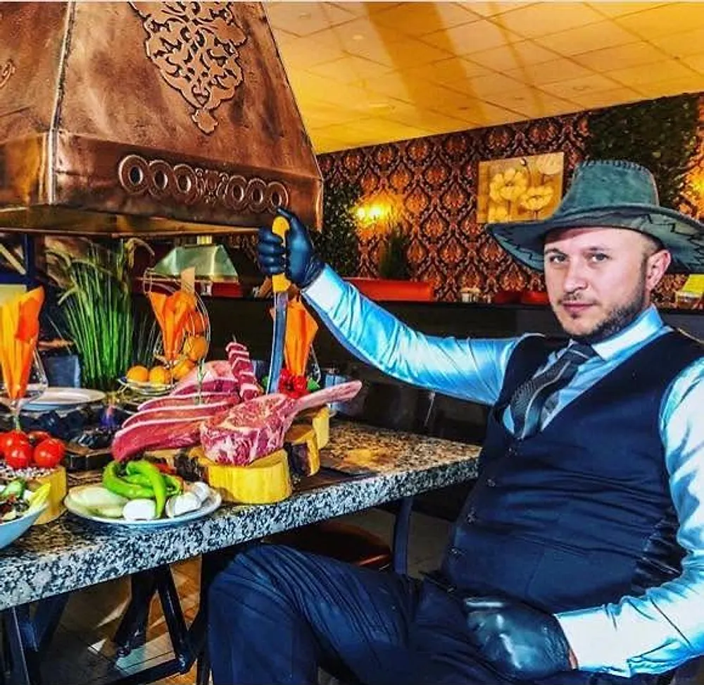 Florya Steak House'un sahibi, şapkasıyla ızgara tezgâhında kemikli etlerin yanında, elinde bıçakla